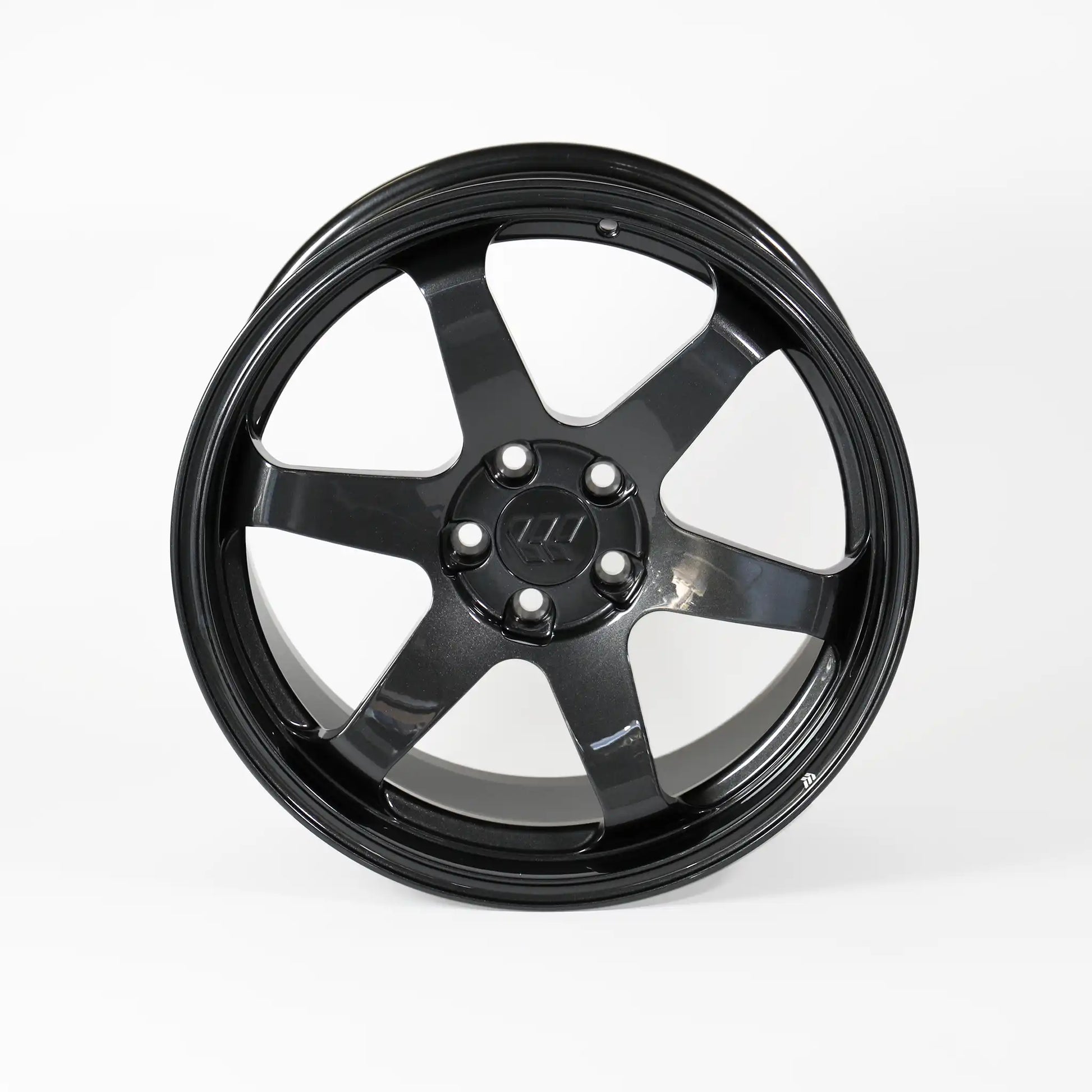 A glossy black multi-spoke alloy wheel rim with a five-bolt center hub, photographed against a seamless light gray studio background.