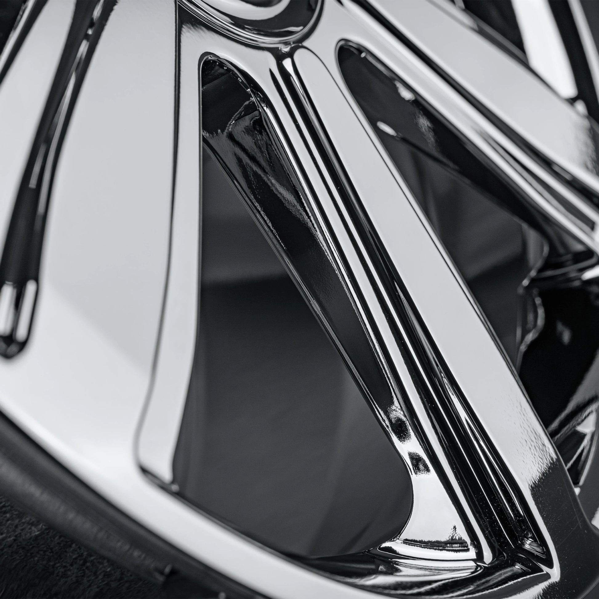 Close-up of a polished chrome multi-spoke car wheel rim showing reflective metallic surfaces and dark recessed areas.
