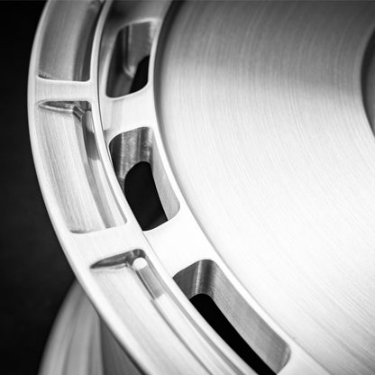 Close-up of a brushed metallic wheel rim with cutout spokes and a dark background.