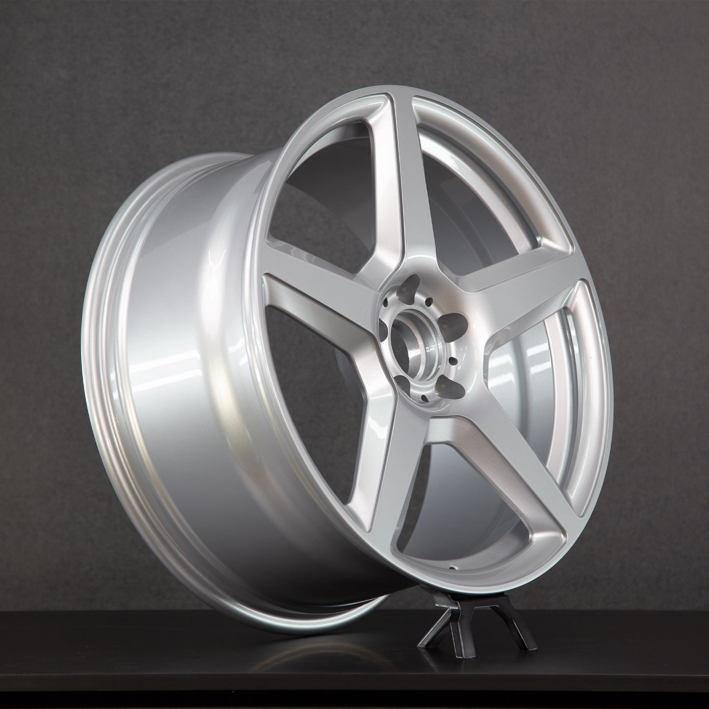 A silver multi-spoke alloy wheel rim displayed on a small stand against a dark gray studio background.