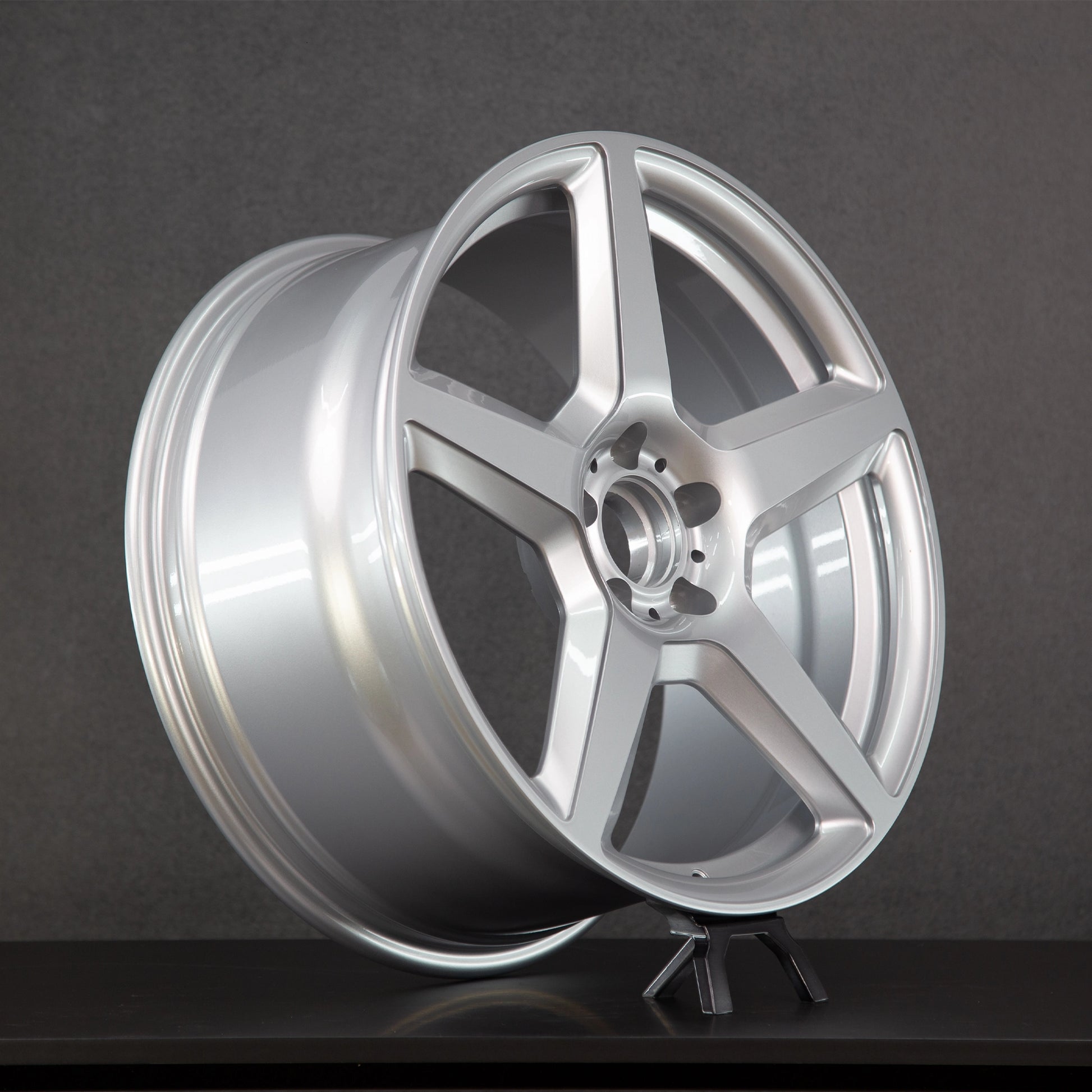 A silver multi-spoke alloy wheel rim displayed on a small stand against a dark gray studio background.