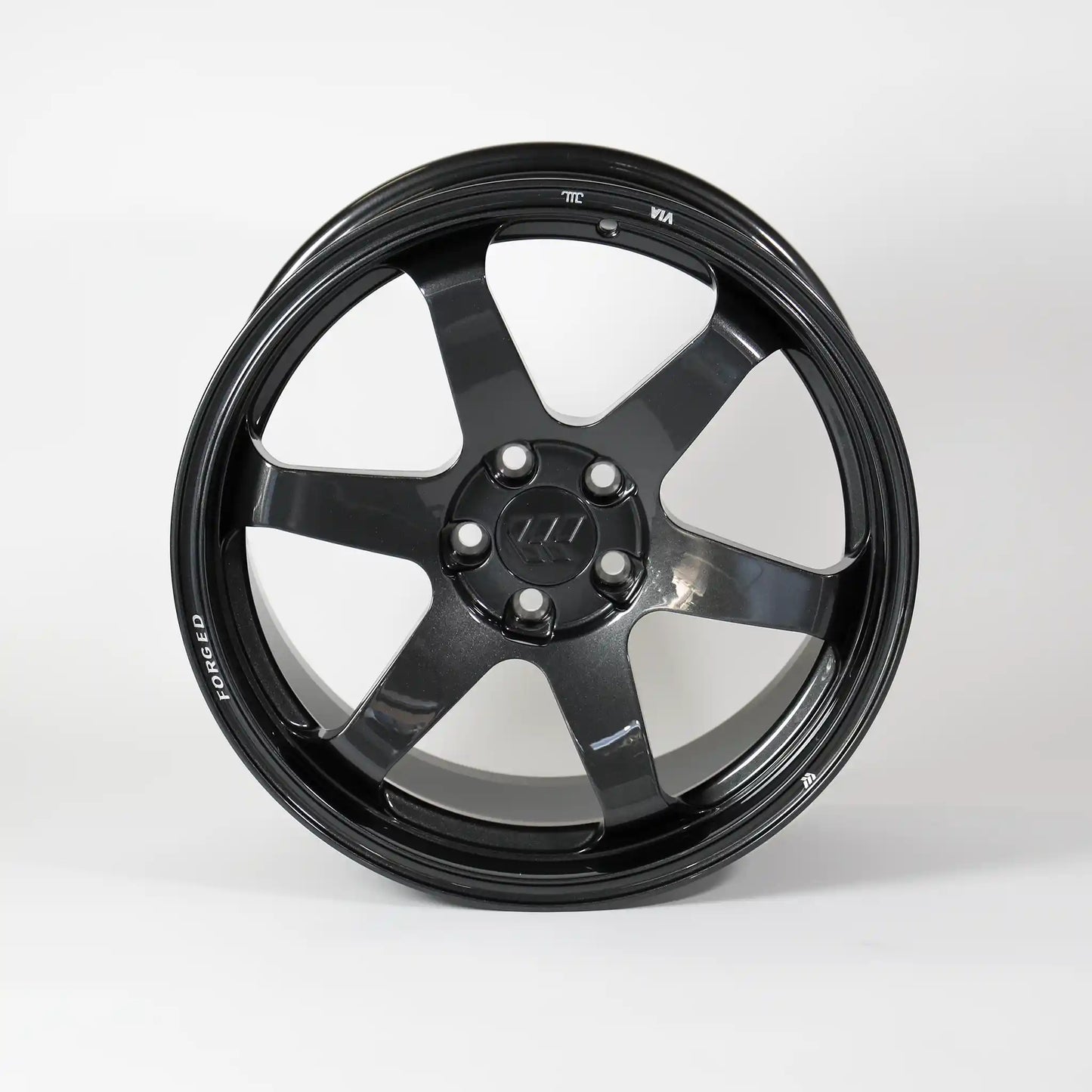 A glossy black multi-spoke alloy wheel rim with a five-lug center cap, photographed against a seamless light gray studio background.