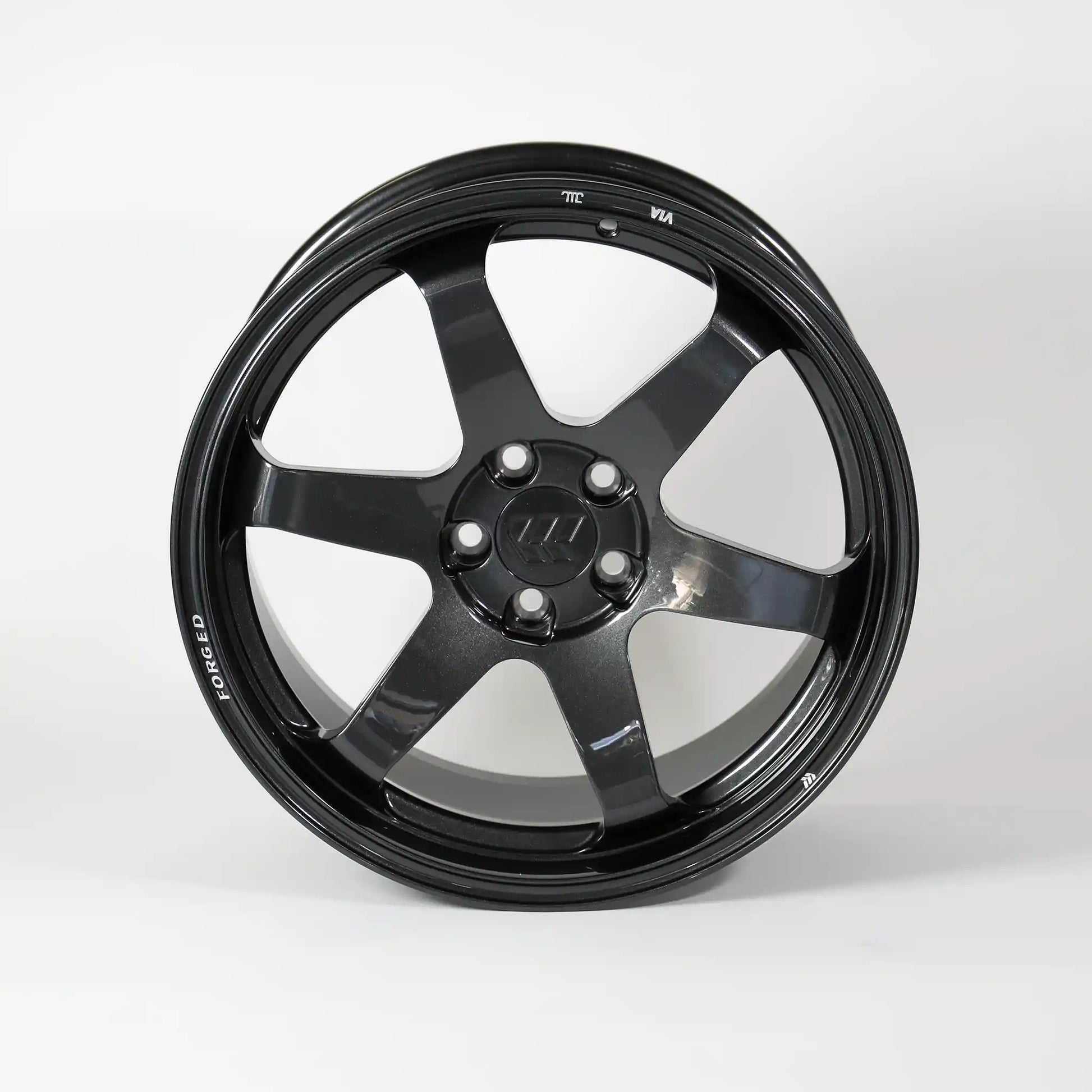 A glossy black multi-spoke alloy wheel rim with a five-lug center cap, photographed against a seamless light gray studio background.